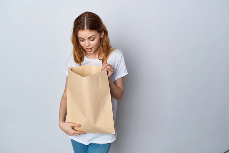 Женщина в белой футболке с пакетом продуктов на светлом фоне