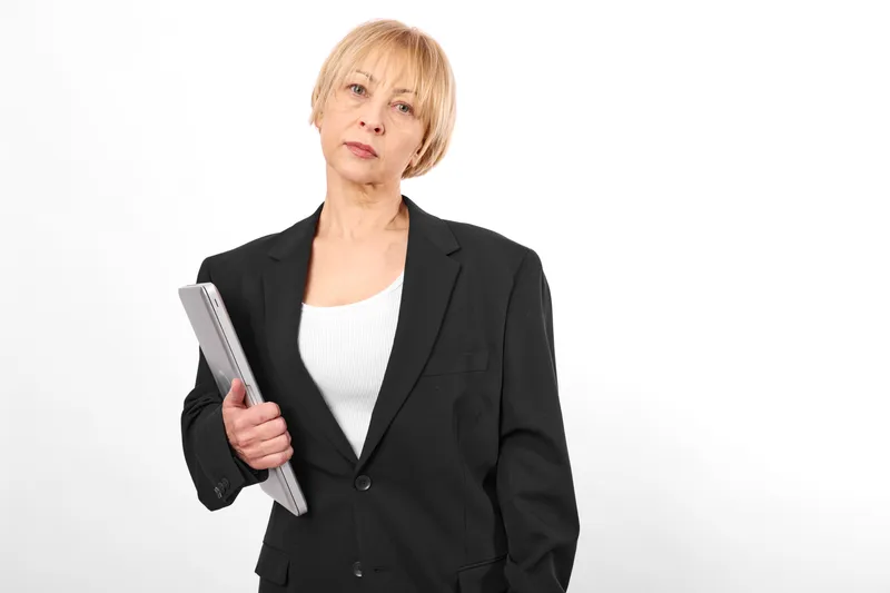 Senior woman in business jacket holds a tablet, worried expression, studio portrait on white background, technology and communication concept for stress concern