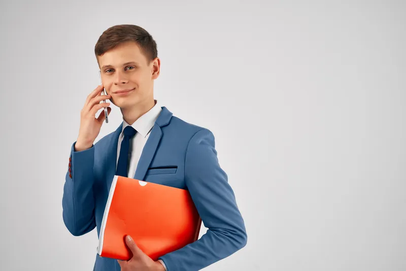 Мужчина в костюме держит в руках красную папку и телефон, используя коммуникационные технологии