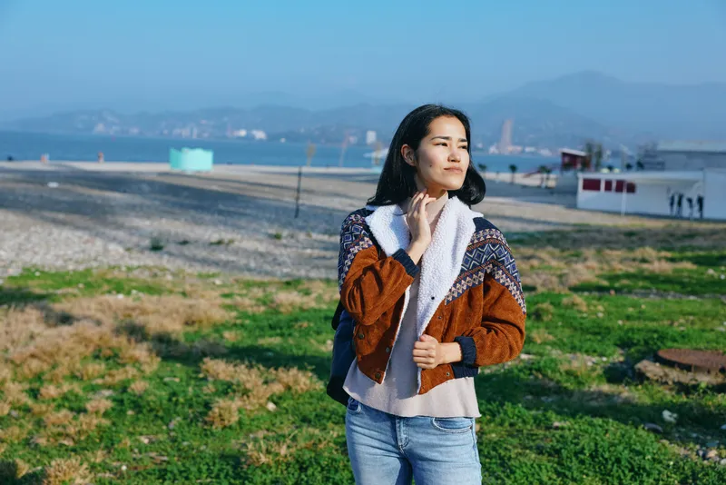 Woman outdoor scarf jacket coastal landscape seaside jeans wind calm fashion travel lifestyle nature horizon field scenery beauty model street casual apparel outfit texture color blue brown green