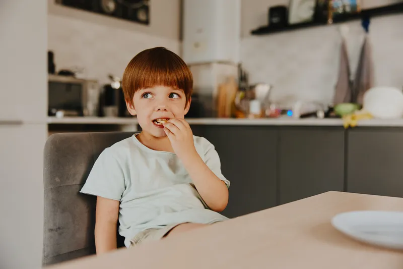 Cheerful boy enjoying a snack in a modern kitchen, surrounded by bright decor and homey details, reflecting a casual and relaxed atmosphere.