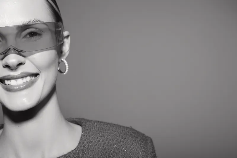 Smiling Caucasian woman with light skin wearing transparent sunglasses and hoop earrings. Close-up portrait with soft lighting and neutral background. Concept of fashion and happiness.