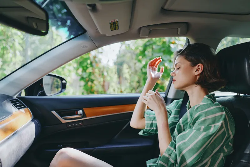 Young woman seated in a stylish car, sipping a beverage while using a vaping device in a relaxed, casual moment.