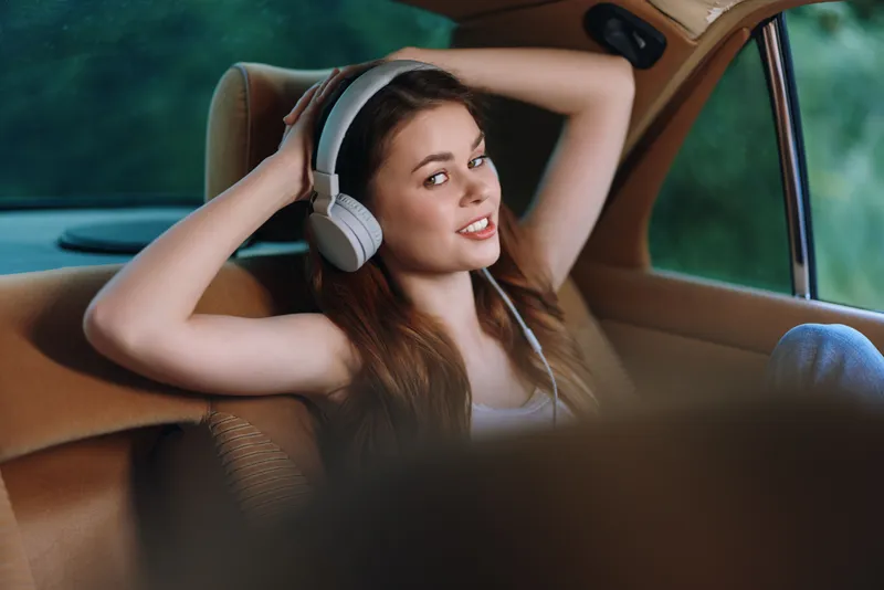 Young woman enjoying music in a car with headphones, relaxed expression, casual style, perfect for portraying leisure and joy in summer.