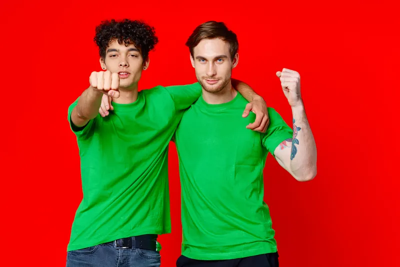 Два веселых друга обнимаются в зеленых футболках, передавая эмоции и общение на красном фоне