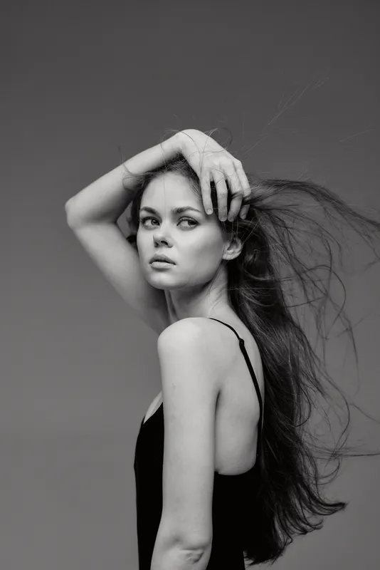 Black and white portrait of a young woman with long hair posing elegantly against a neutral background.