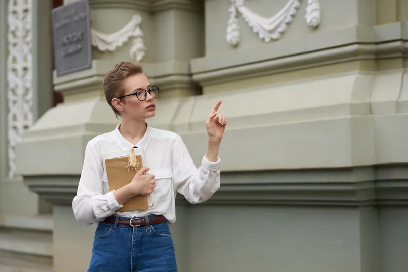 Студент в очках прогуливается по городу с книгой в руках, посвящая время образованию