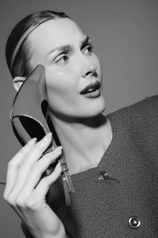 Close-up of a fair skinned caucasian woman holding a high heel shoe near her face in a studio. Concept of fashion, style, and elegance with monochrome lighting.