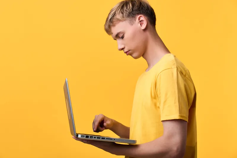 Laptop, education, youth, technology, computer, device, focused learner engages with a laptop against a bright yellow backdrop, showcasing digital work, online tasks, and creative problem solving in