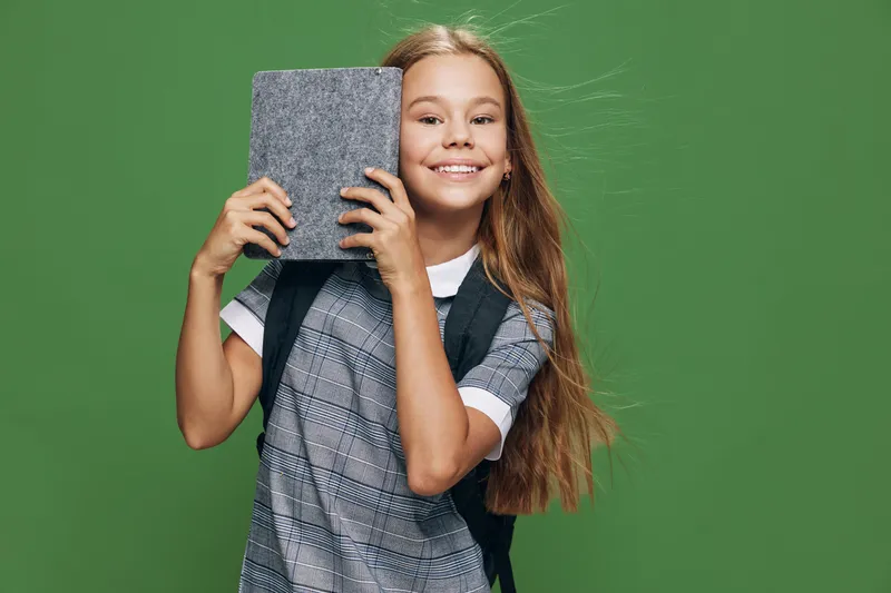 Girl child smiling and holding closed book on green background for education and learning. Long hair, casual clothes with happy face and knowledge concept in studio.