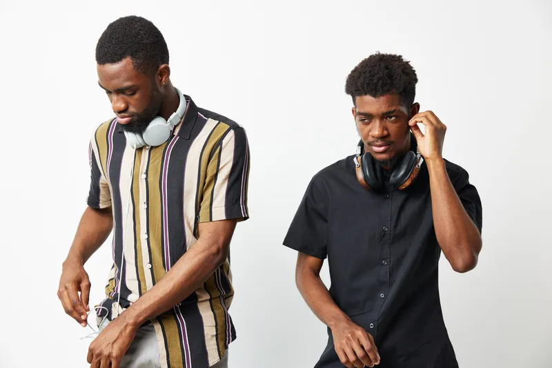 Two African American men wearing headphones engaged in music, showcasing a casual and stylish vibe. Their unique outfits reflect contemporary fashion trends.