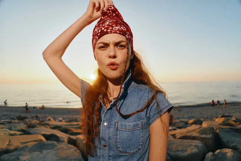 Lifestyle woman in modern boho-western denim street style with a red bandana, casual look, and film color sunset background by the beach.