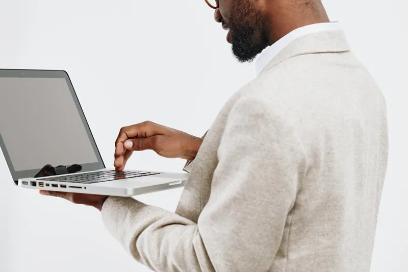Man working on laptop computer in beige suit jacket isolated on plain white background, close-up. People business concept, technology, professional.