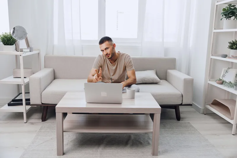 Engaged man working on laptop at home, showcasing a modern living space with natural light and minimalist decor, conveying productivity and comfort.