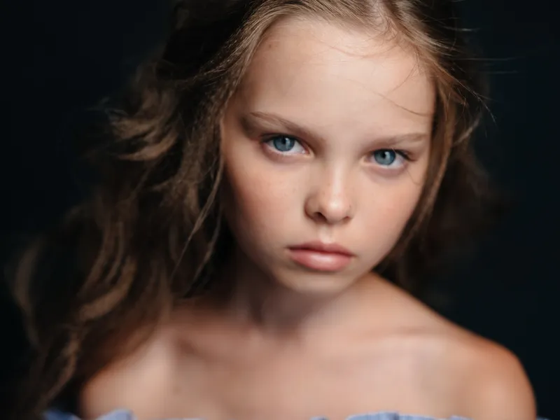 Красивая голубоглазая девушка с обнажёнными плечами на тёмном фоне и вьющимися волосами