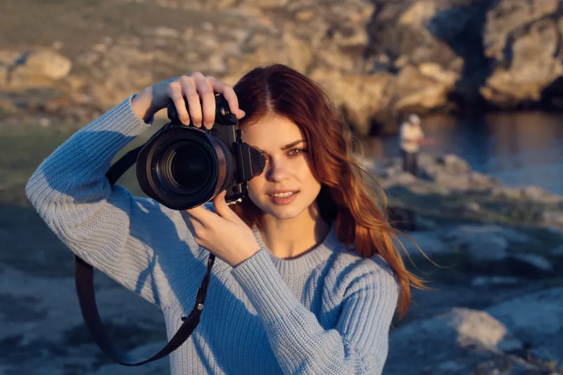Рыжеволосая женщина-фотограф на фоне скалистых гор