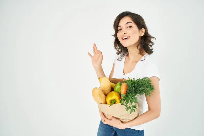 Симпатичная брюнетка в белой футболке с пакетом продуктов жестикулирует рукой в супермаркете