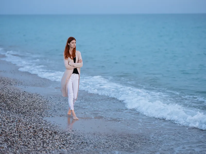 Женщина на пляже у океана с прозрачной водой, в свитере, позирует для фото
