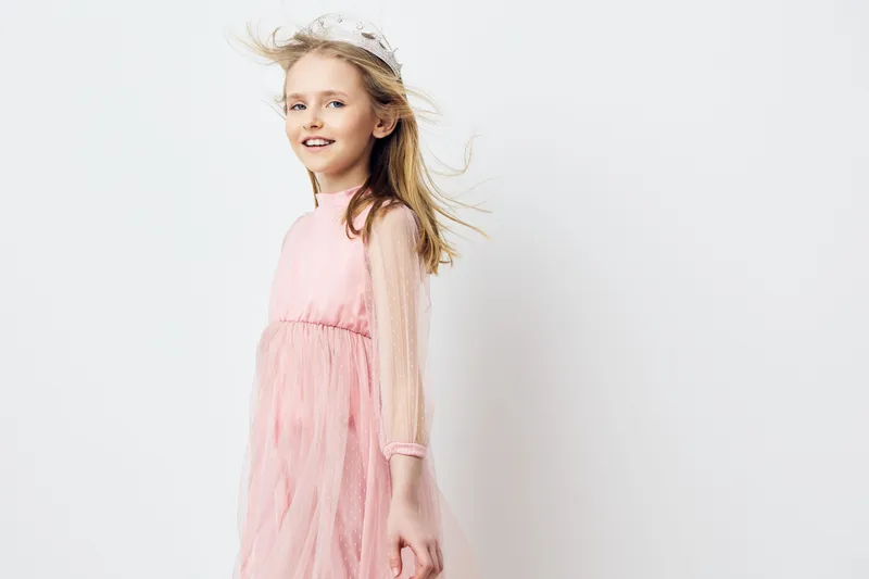 Joyful little girl in a pink tulle dress, smiling and twirling against a soft white background, embodying childhood innocence and happiness in a bright and airy setting