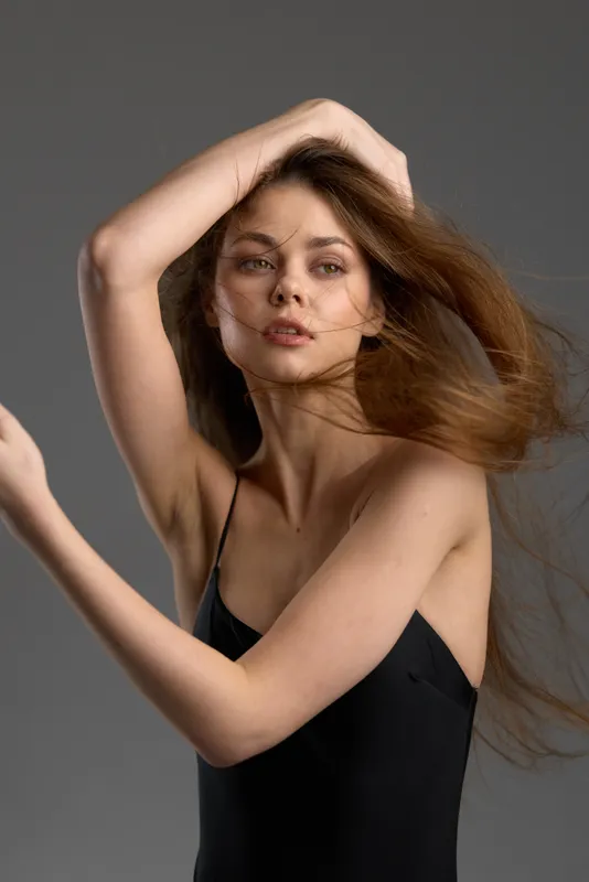 Young woman with long hair posing in elegant black dress with dynamic movement and confident expression