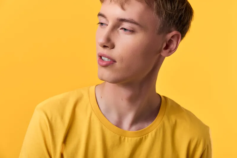 Yellow shirt, young man, studio lighting, contemplative look, fashion pose, minimal background, soft shadows, bold colors, modern style for fashion photography