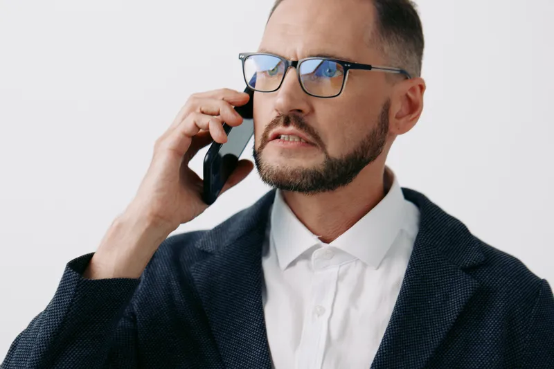 A professional businessman on a phone call, isolated on a white background. He looks focused, serious, and confident, signaling clear communication and corporate urgency.
