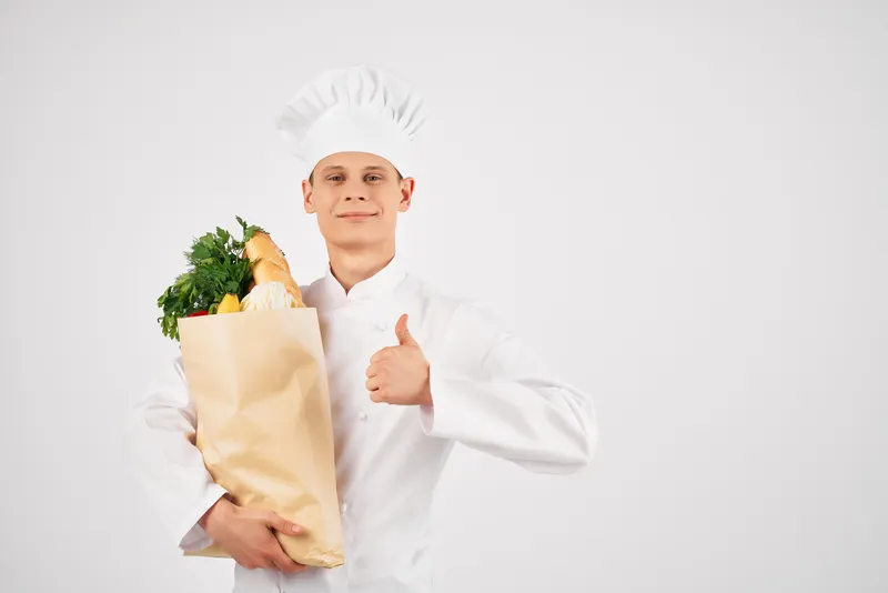 Весёлый шеф-повар-мужчина с упаковкой полезных продуктов предоставляет услуги на кухне