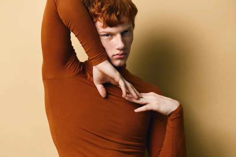 Redhead man posing with stylish hand gestures in brown turtleneck sweater on beige background for fashion, portrait, model and expression concept in studio lighting.