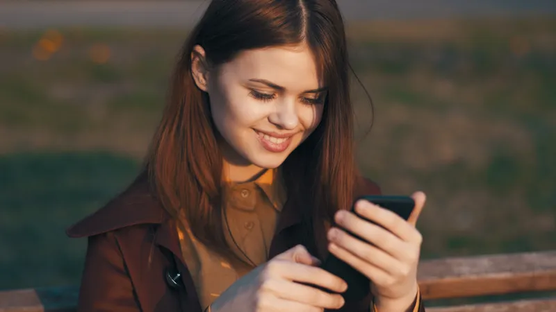 Весёлая женщина в парке сидит на скамейке с телефоном в руках, общение