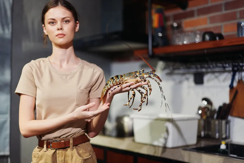 Молодая женщина держит омара на кухне, готовясь приготовить вкусное блюдо из морепродуктов