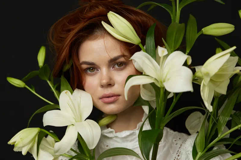 Elegant young woman with auburn hair surrounded by white lilies, conveying serenity and beauty, ideal for concepts related to nature and floral themes