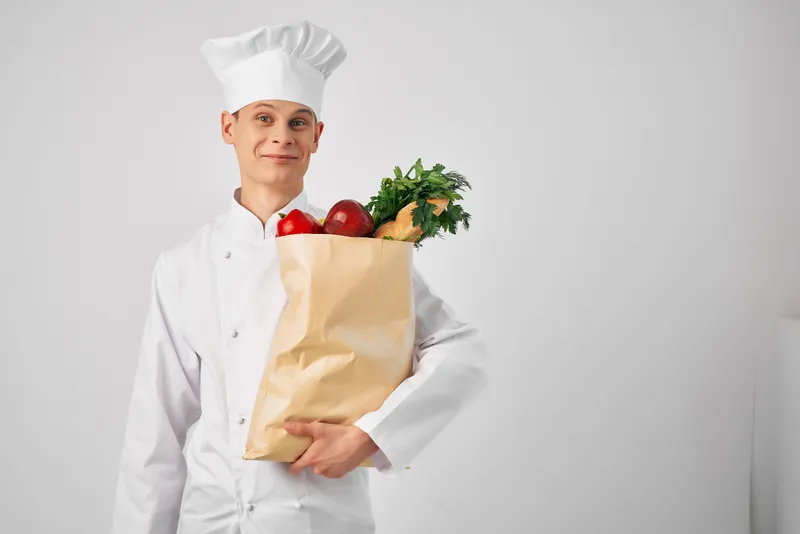 Мужчина в униформе шеф-повара занимается упаковкой продуктов для службы доставки еды, готовит здоровую пищу