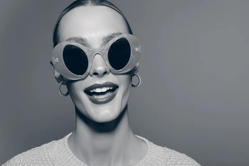 Smiling caucasian woman with pale skin wears large round sunglasses and hoop earrings in studio portrait. Fashion concept.