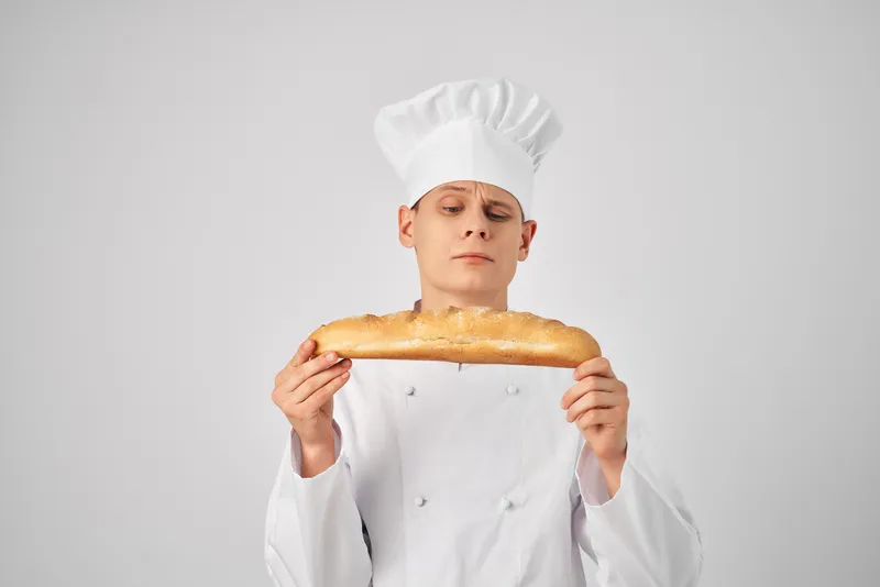 Мужчина в одежде повара, профессионал, с багетом в руках — свежий продукт, работа