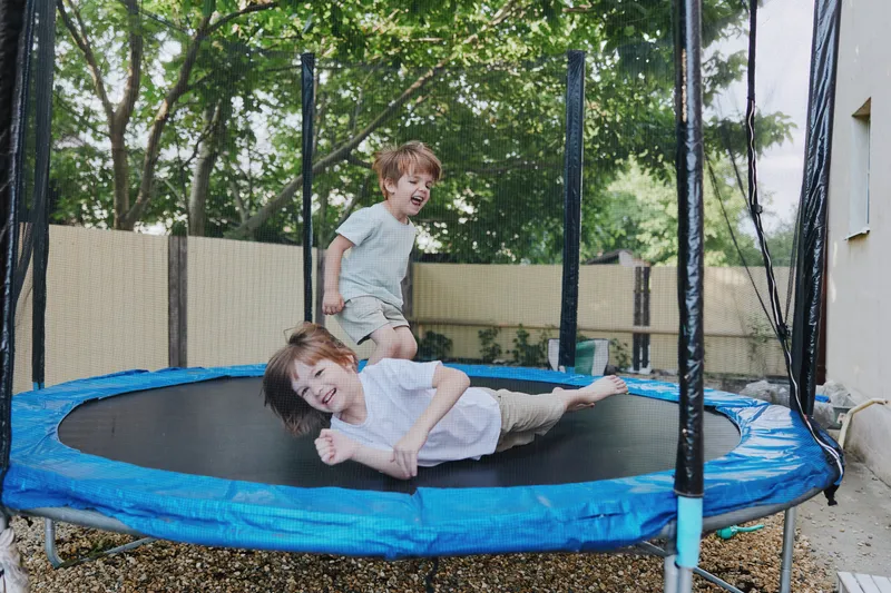 Happy boys playing on a trampoline, enjoying a sunny day outdoors with laughter and excitement in a vibrant green setting.