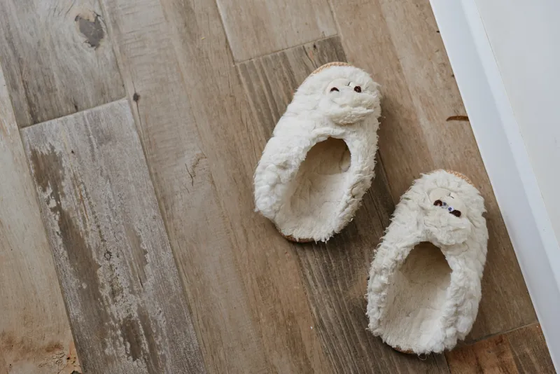 Cozy indoor scene shows fluffy slippers resting on a warm wooden floor, creating a quiet inviting moment of home comfort and relaxation.