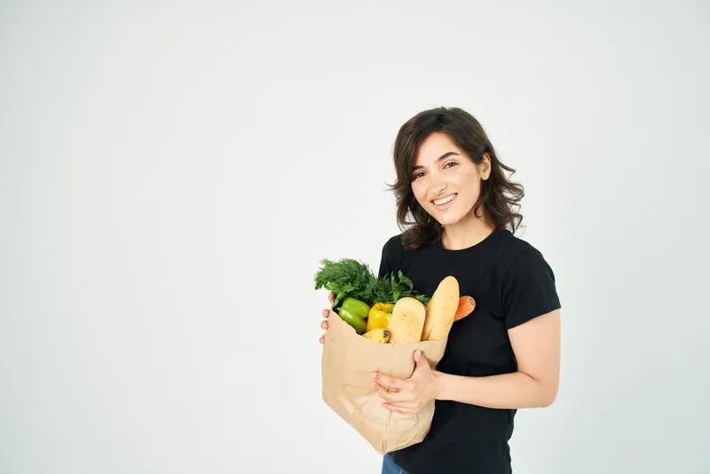 Милая брюнетка с пакетом продуктов в супермаркете, овощи
