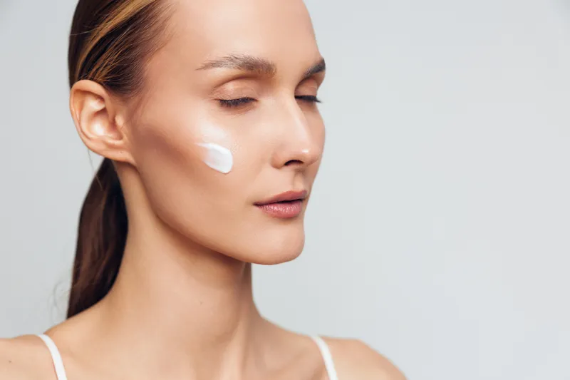 Woman applying white face cream, side profile closeup on clean neutral background, soft studio lighting, skincare routine, beauty care, wellness concept, self care calm mood today