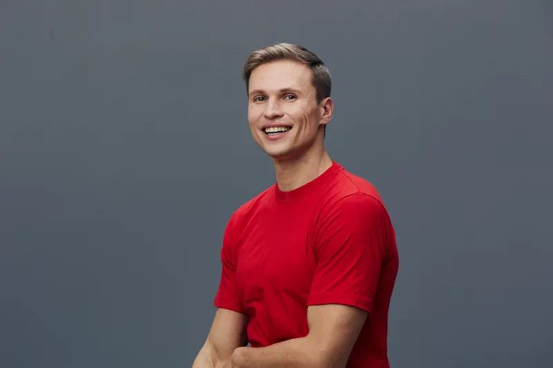Smiling man wearing red t-shirt looking happy cheerful confident pose studio portrait blue background. People lifestyle concept