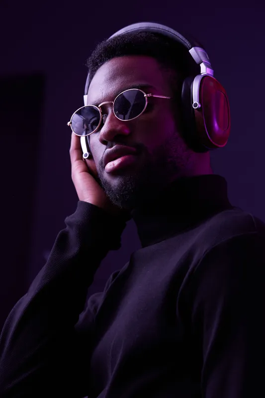 Stylish man with headphones in sunglasses, expressing confidence and passion for music, set against a purple and black background, showcasing a modern and artistic vibe