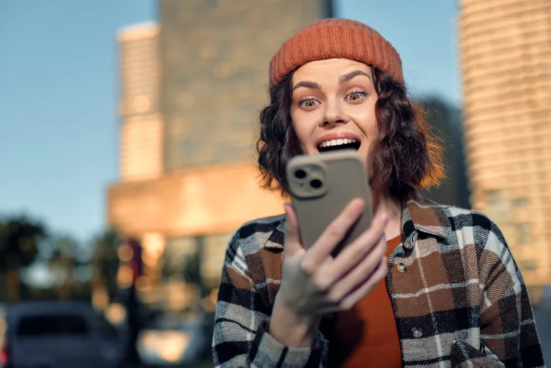 Woman phone surprised urban candid portrait during golden hour, candid happiness and authenticity, emotional storytelling and mindful living in modern city lifestyle scene.