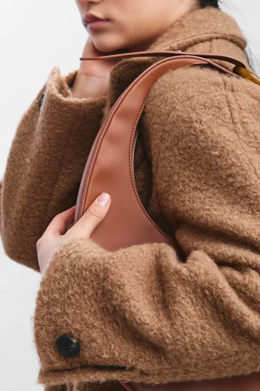 asian woman in a warm brown wool coat carries a leather bag in a modern urban setting, exuding effortless style and confidence, with soft lighting highlighting textures and chic fashion details.