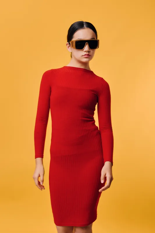 Woman in red dress and sunglasses posing against orange background studio. Fashion model with stylish outfit and confident expression in modern clothing photography.