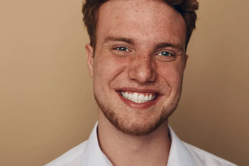 Close-up portrait of a smiling young man with freckles and red hair on beige background. Concept of happiness, confidence, and natural beauty in casual style.