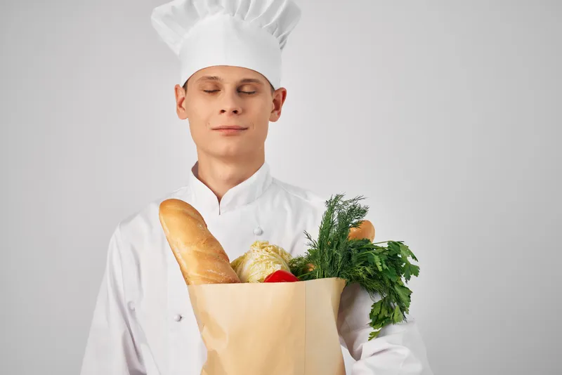 Мужчина в одежде шеф-повара с упаковкой продуктов готовит еду на кухне
