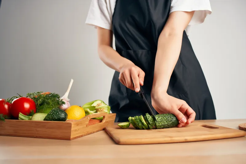 Домохозяйка в черном фартуке на кухне готовит витаминный салат