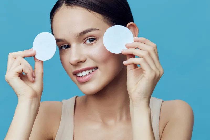 Young woman smiling with skincare pads on a blue background, representing beauty and self care Emotionally engaging and perfect for health related themes