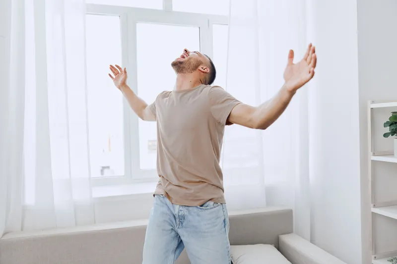 Energized man celebrating personal freedom and emotional well-being in a bright room, embracing vulnerability and the journey of self-discovery and acceptance.