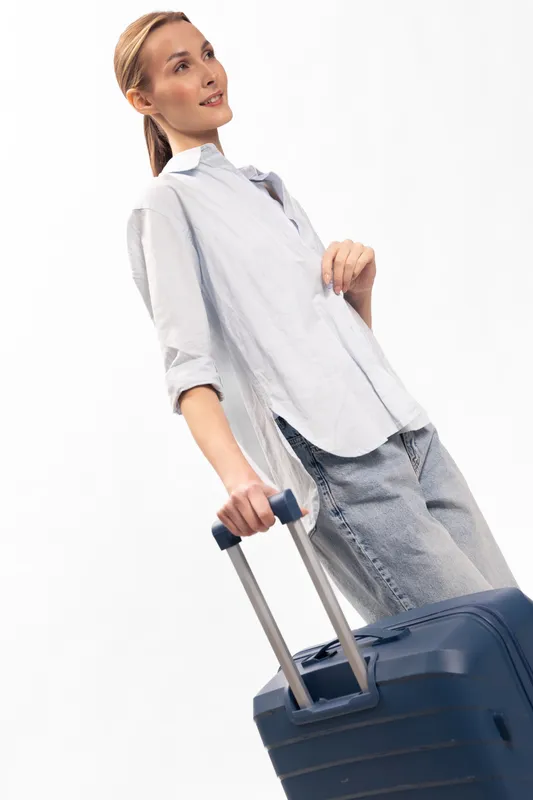 Young woman in casual clothes holds suitcase handle and looks away with slight smile. Concept of travel, vacation preparation, and light packing for trip or business journey.