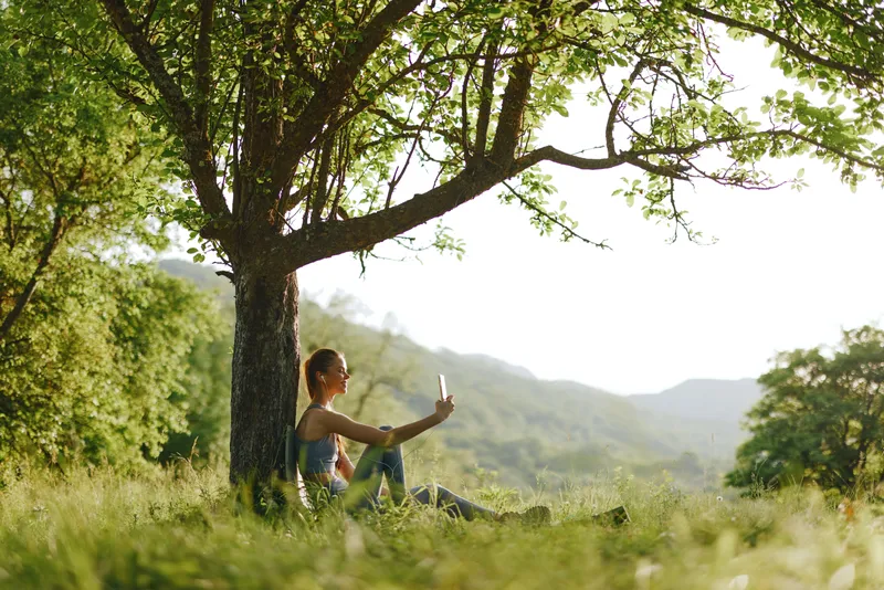 A young woman enjoying relax time under a tree in a sunny nature setting, embodying tranquility and connection with the environment on a bright day
